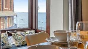 A dining area with a view of the water, a table set with bowls and glasses, and patterned pillows. - 2 Bed in Swanage (oc-wy547) (Swanage)