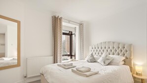 A bedroom with a large bed, a mirror, a radiator, and a window with curtains. - 2 Bed in Swanage (oc-wy547) (Swanage)