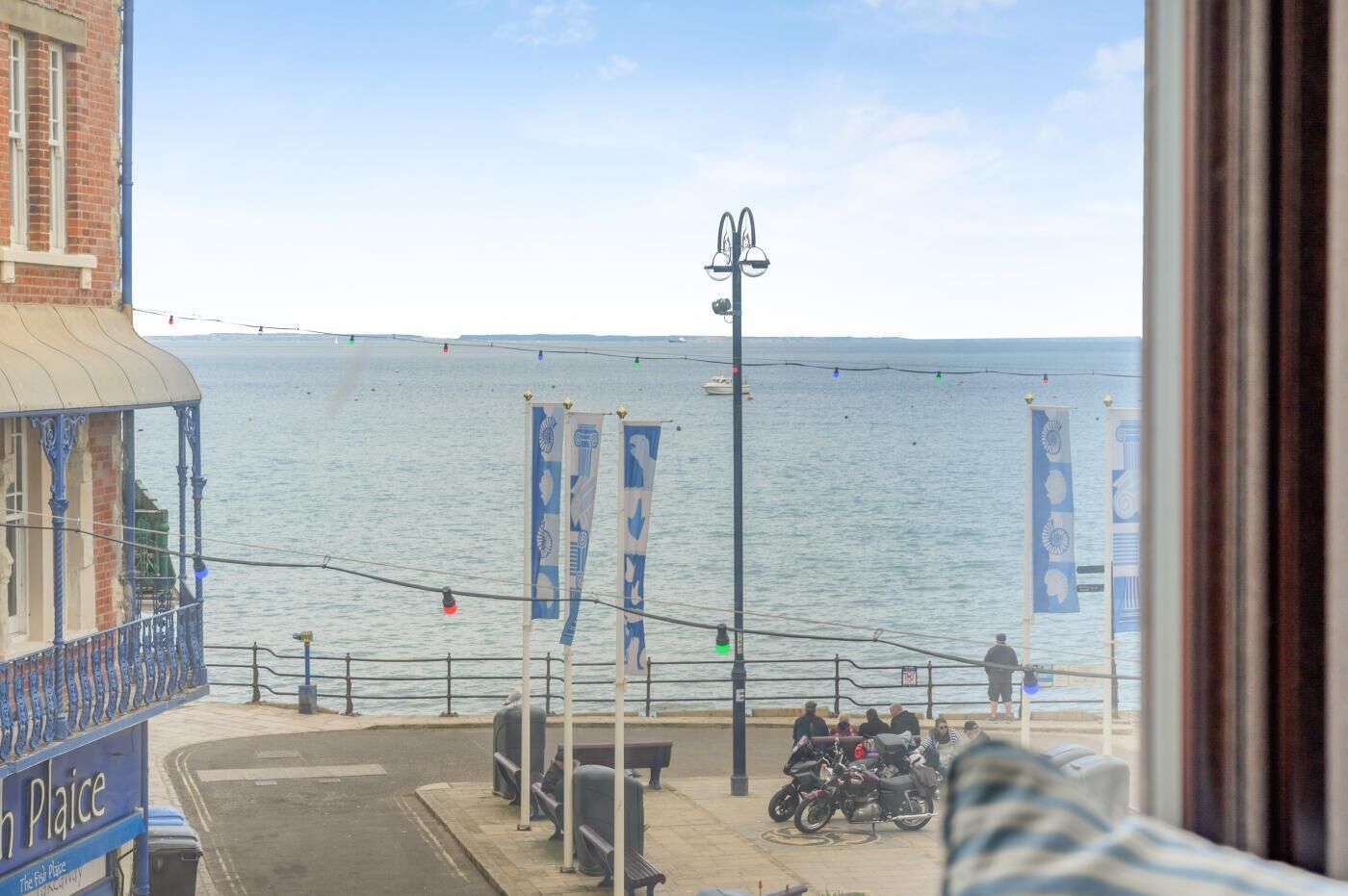 A waterfront view with a building, a pier, and a row of flags.