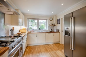 A modern kitchen with a stainless steel refrigerator, a built-in oven, and a window with a view of greenery outside.