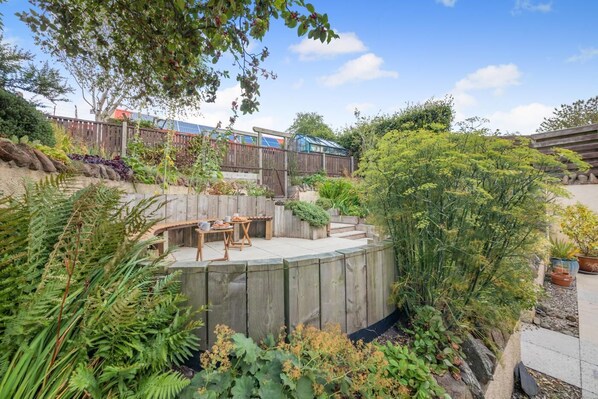 A backyard with a wooden deck, outdoor seating, and various plants.