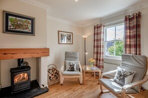 A cozy living room with a fireplace, two chairs, a table with a vase, and a window with curtains. - 5 Bed in Swinton (oc-t32750) (Swinton)