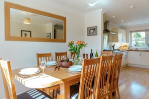 A dining room with a wooden table, chairs, a large mirror, and a vase with flowers.