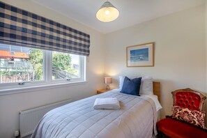 A bedroom with a bed, a window with a checkered blind, a bedside table with a lamp, a red upholstered chair, and a framed picture on the wall. - 5 Bed in Swinton (oc-t32750) (Swinton)