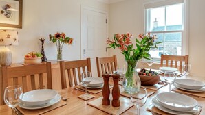 Een eettafel gedekt voor vier personen, met witte borden, glazen en een vaas met bloemen.