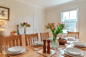 A dining table set for four with white plates, glasses, and a vase of flowers.