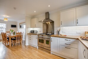 A modern kitchen with white cabinets, stainless steel appliances, and a wooden dining table set for four. - 5 Bed in Swinton (oc-t32750) (Swinton)