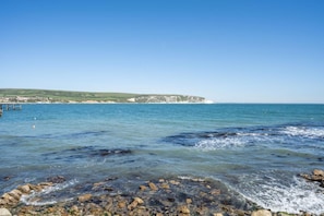 A coastal landscape with clear blue water, rocky shoreline, and a distant cliff. - 2 Bed in Swanage (oc-wy500) (Swanage)
