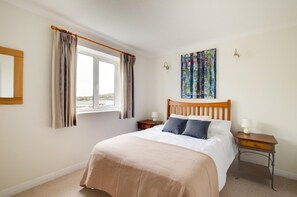 A bedroom with a bed, a window, curtains, a bedside table, a lamp, and a painting on the wall. - 2 Bed in Swanage (oc-wy500) (Swanage)