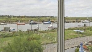 Blick auf einen Yachthafen mit vertäuten Booten, eine Rasenfläche und eine Terrasse mit Gartenmöbeln.