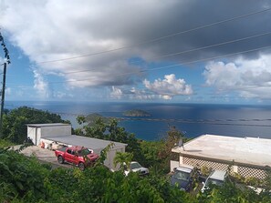A coastal view with a red SUV parked in a driveway, surrounded by greenery and buildings.