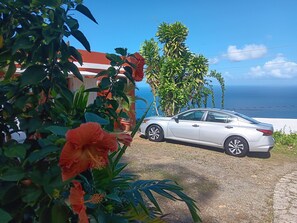 A white car parked in front of a house with a view of the ocean.