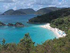A beach with clear turquoise waters, a sandy shore, and lush green hills in the background.