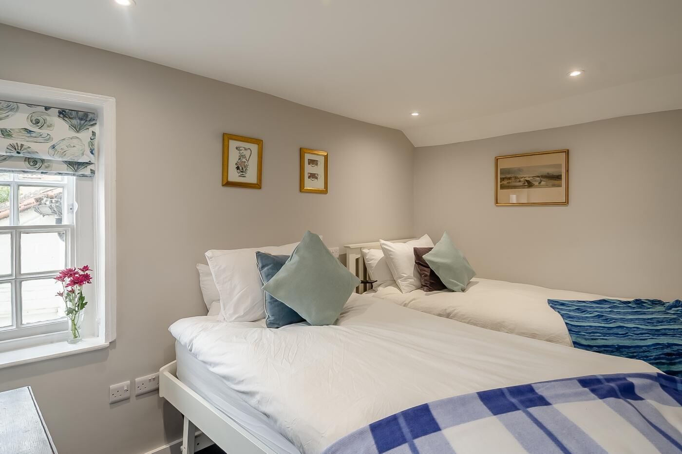 A bedroom with two beds, a window with a view, and framed pictures on the wall.
