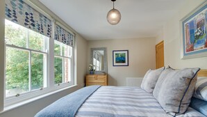 Ein Schlafzimmer mit Bett, Kommode, Heizkörper und Fenster mit Blick auf Bäume.