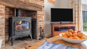 Un salon chaleureux avec une cheminée en briques, un téléviseur à écran plat posé sur un meuble en bois et un panier rempli d’oranges sur la table.