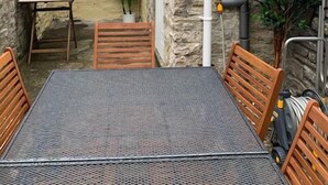 Un edificio de piedra con un pequeño patio que tiene una mesa de metal y sillas de madera.