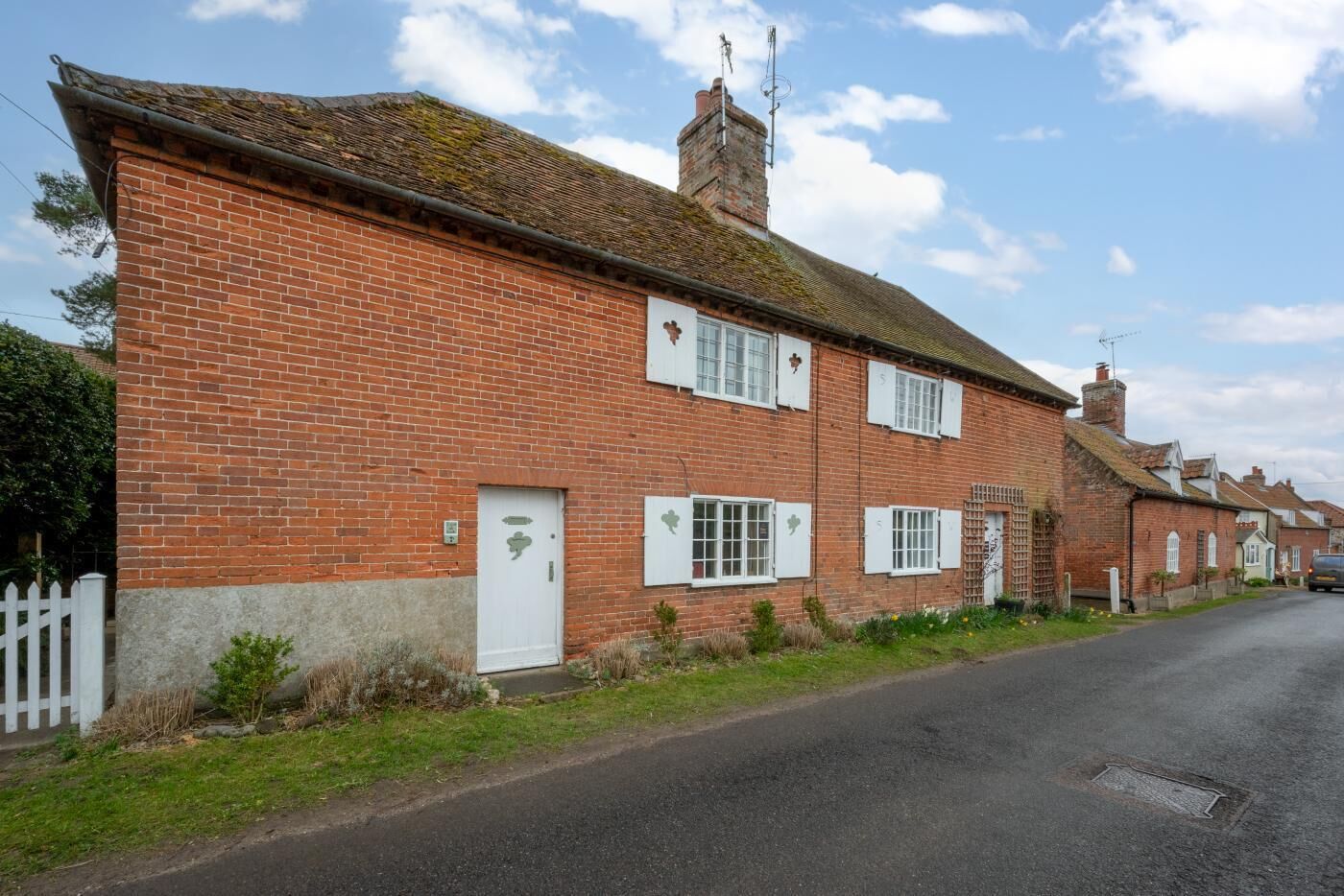 A two-story brick house with a white door and shutters, a chimney, and a small garden area.
