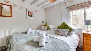 Ein gemütliches Schlafzimmer mit zwei Betten, einem Heizkörper, einem Fenster mit Vorhängen und einer Lampe auf einem Nachttisch.