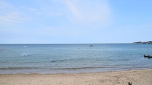 En strand med roligt vand, sandet bredde og en klar himmel.