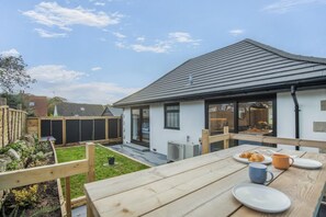 A patio with a table set for breakfast, a garden, and a house with a dark roof and white walls. - 2 Bed in Swanage (oc-h33032) (Swanage)