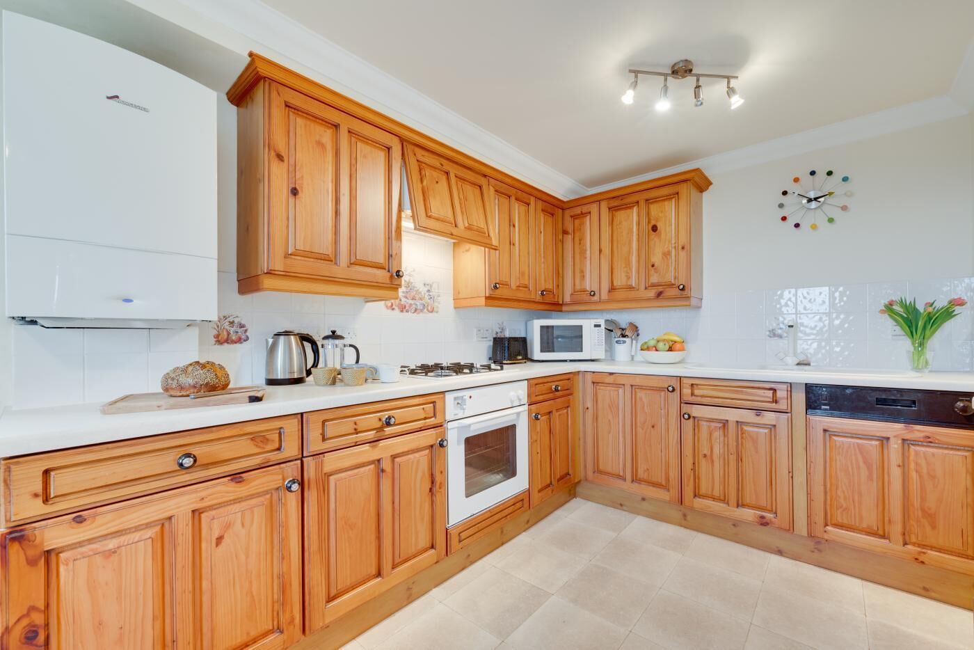 Una cocina moderna con armarios de madera, encimeras blancas, microondas, horno y fregadero.