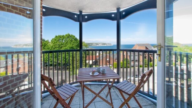 Un balcon avec une table et des chaises, offrant une vue panoramique sur la côte et les bâtiments.