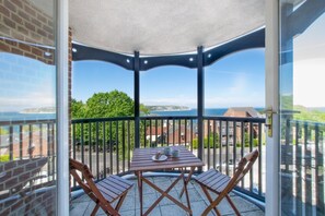 Un balcon avec une table et des chaises, offrant une vue panoramique sur la côte et les bâtiments.