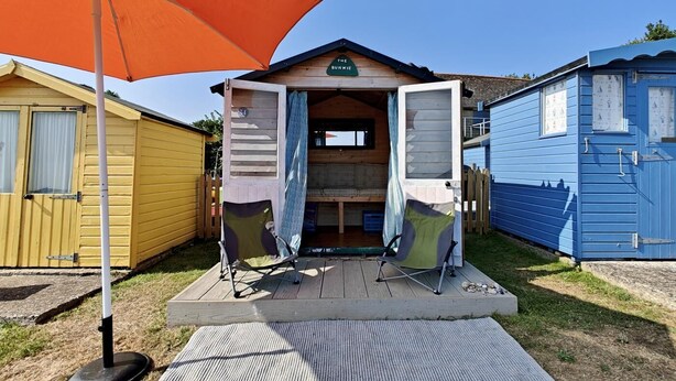 A small wooden structure with an open door, a picnic table, and an orange umbrella in front. - 3 Bed in Bembridge (oc-s33085) (Bembridge)