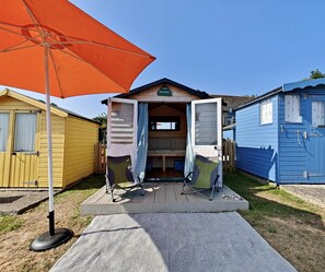A small wooden structure with an open door, a picnic table, and an orange umbrella in front. - 3 Bed in Bembridge (oc-s33085) (Bembridge)
