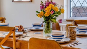 A dining table set with blue-striped bowls, a vase of yellow and pink flowers, and a jar of grains. - 3 Bed in Bembridge (oc-s33085) (Bembridge)