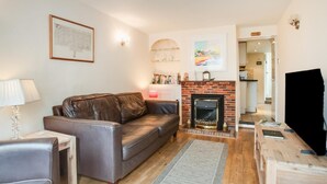 A living room with a leather sofa, a fireplace, a television, and a bookshelf. - 2 Bed in Southwold (oc-hsc) (Southwold)