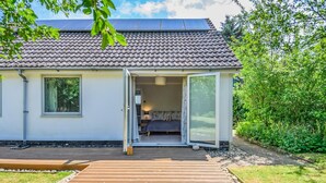 Ein modernes Haus mit Ziegeldach, einer Holzdiele und einem großen Schiebeglastür, die zu einem Schlafzimmer mit Bett und Nachttisch führt.