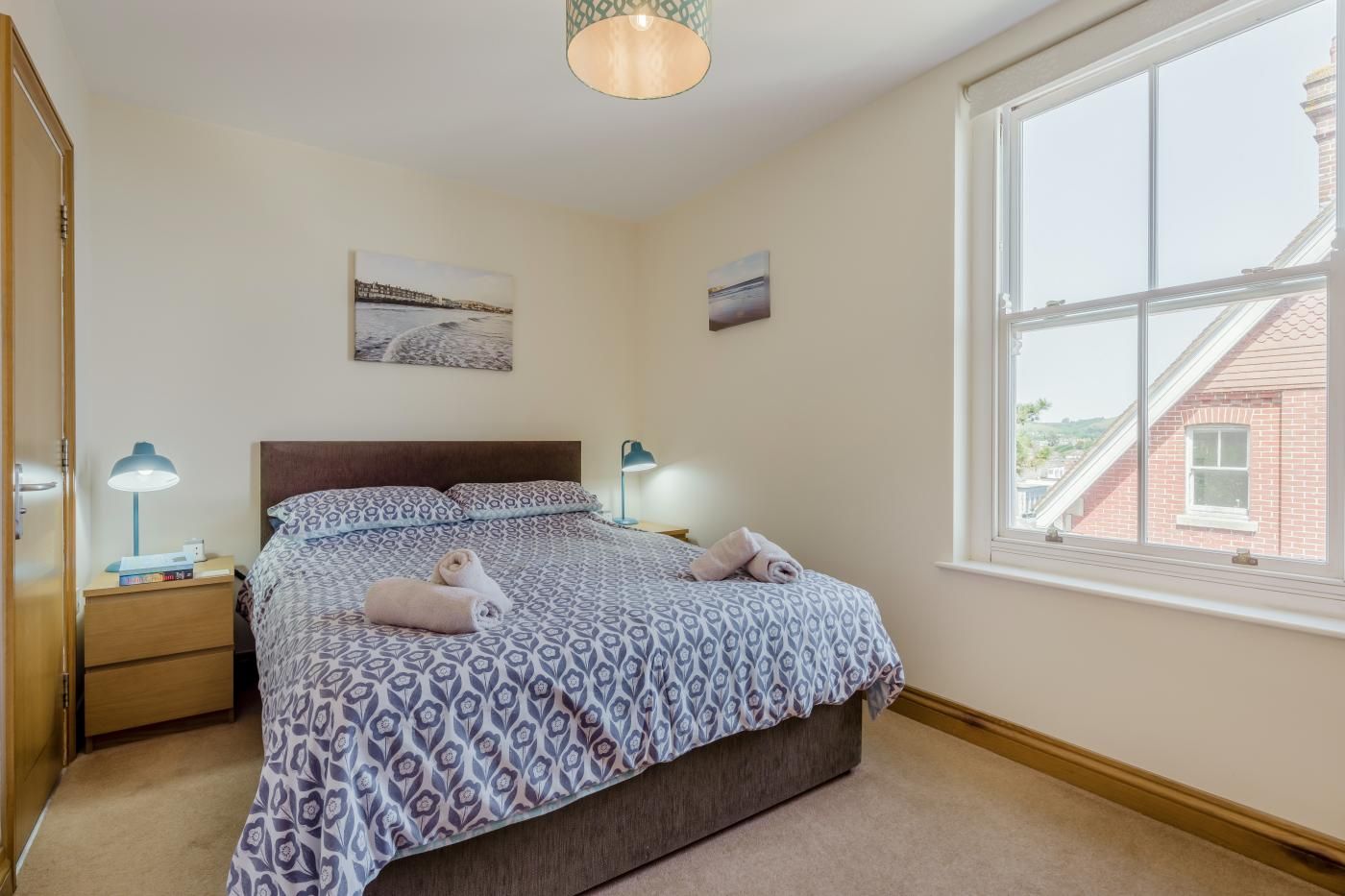 A bedroom with a bed, two bedside tables, a window, and artwork on the wall.