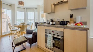 Une cuisine moderne dotée d’un four encastré, un coin repas avec une table et des chaises, et de grandes fenêtres offrant une vue dégagée.