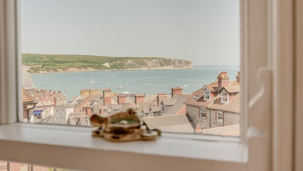 Vue d ’une ville côtière depuis une fenêtre, avec une petite figurine posée sur le rebord.