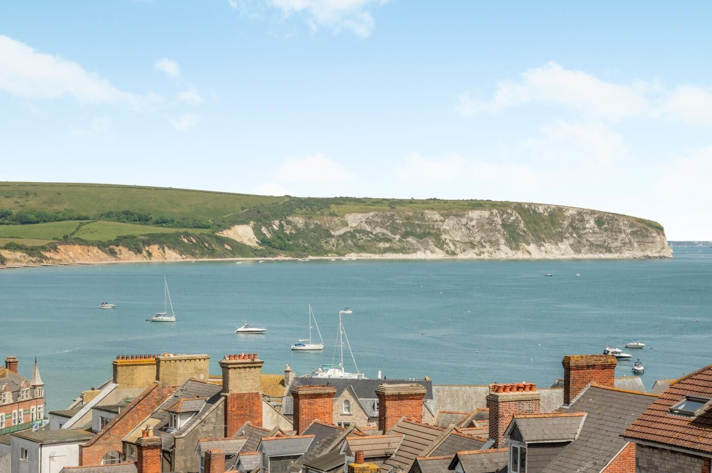 A coastal town with terraced houses, a cliff, and boats in the water.