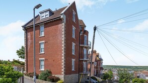 Un bâtiment en briques rouges, doté de nombreuses fenêtres et de balcons, une allée pavée et une vue dégagée sur les environs.