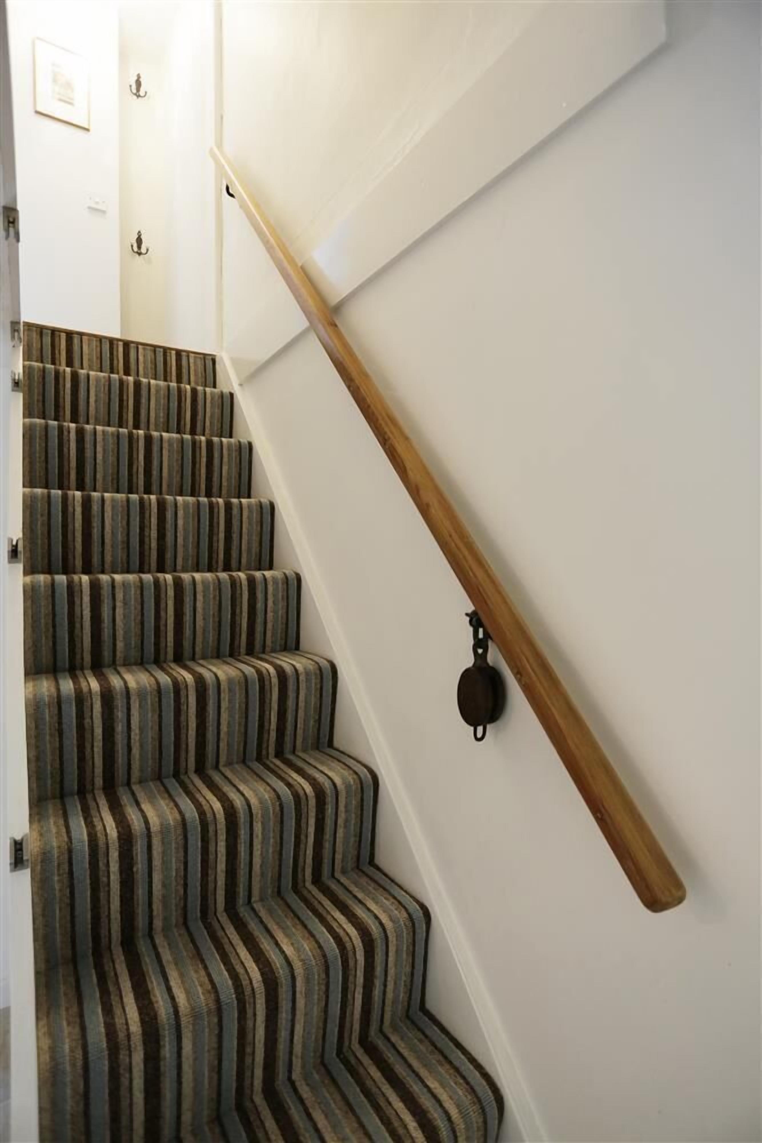 Een trap met gestreept tapijt, een houten leuning en een wandlamp.