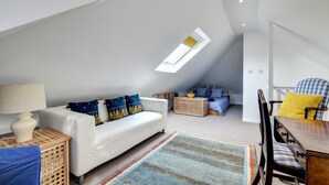 Un dormitorio tipo loft con techo inclinado, un sofá blanco, una mesa de comedor y una silla a cuadros.