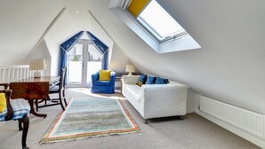 Un espacioso dormitorio en el ático con un tragaluz, un sofá blanco, un sillón azul y una silla de madera.