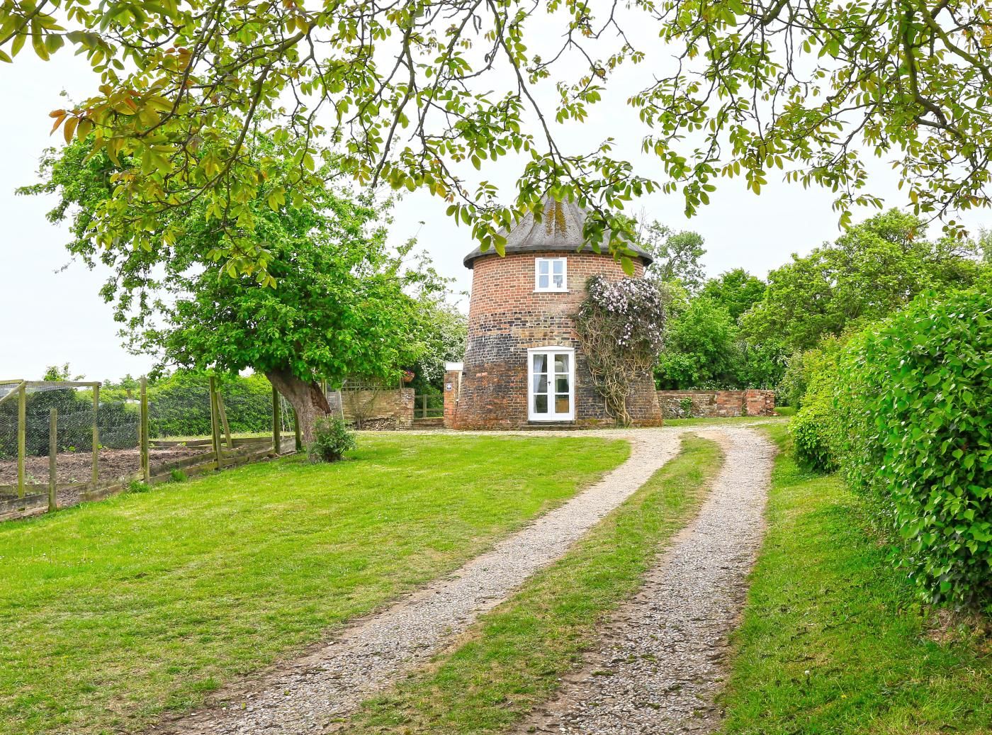 A brick tower house with a gravel path leading to it, surrounded by greenery.