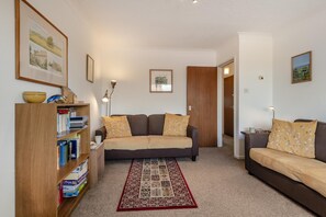 A cozy living room with a sofa, a bookshelf, a patterned rug, and framed pictures on the walls. - 2 Bed in Swanage (oc-wy356) (Swanage)