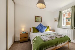 Ein Schlafzimmer mit Bett, Nachttischen, einer Lampe, einem Gemälde und einem Fenster mit Vorhängen.