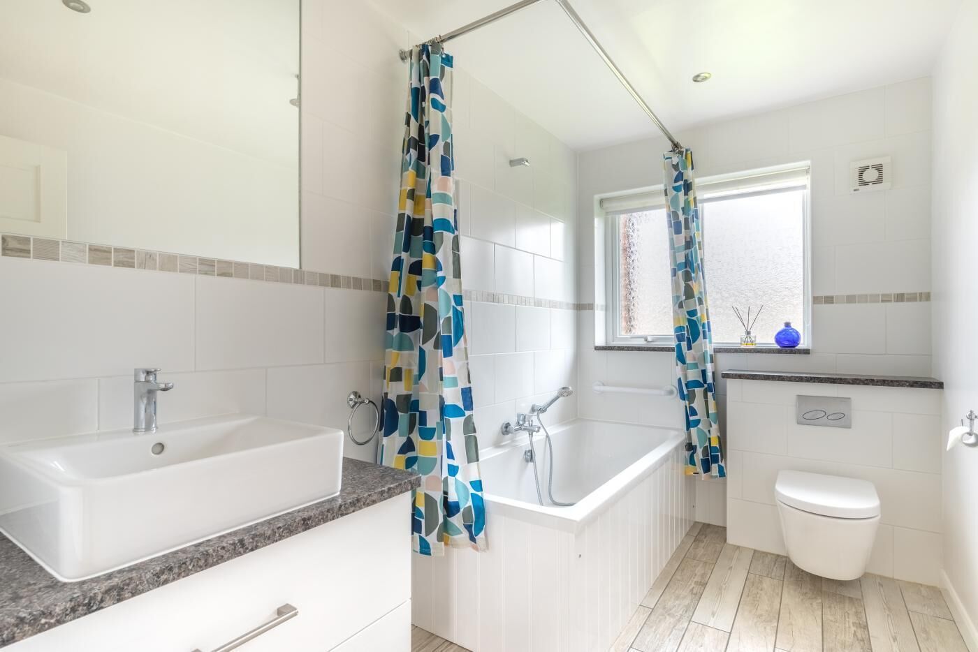 A modern bathroom with a bathtub, a shower with a curtain, a toilet, and a window.
