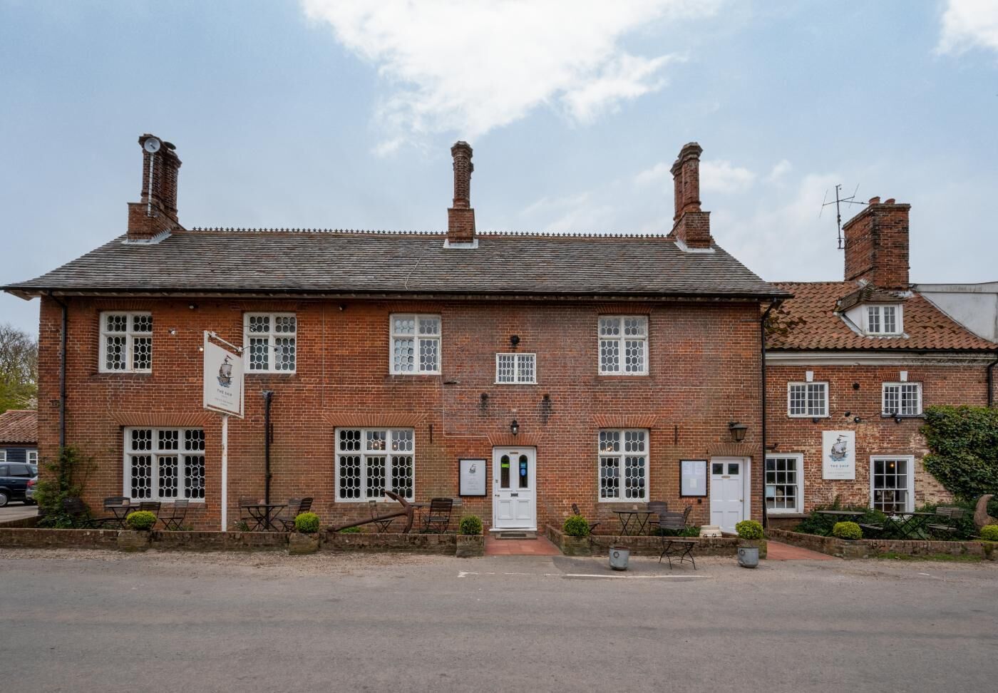 A traditional brick building with multiple chimneys, a central door, and several windows with white frames.