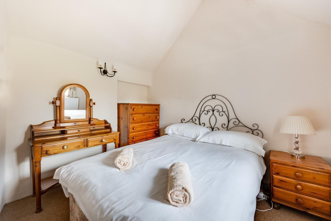 A bedroom with a bed, a wooden dresser, a nightstand, and a mirror.