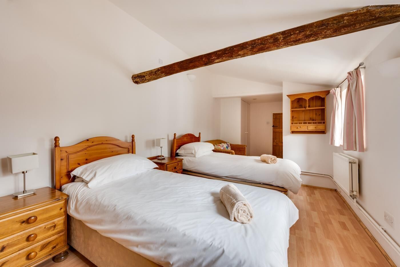 A hotel room with two wooden beds, a wooden dresser, a nightstand, and a wooden ceiling beam.