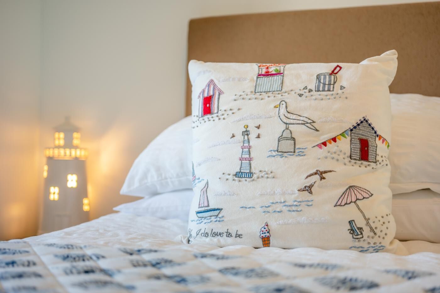 Un lit avec un oreiller blanc orné d’illustrations sur le thème maritime, représentant un phare et un voilier.