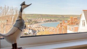 Eine Vogelstatue auf einem Fensterbrett mit Blick auf eine Küstenstadt, Gebäude und einen Strand.